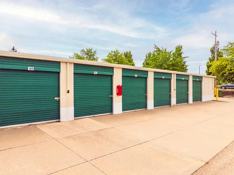 Drive-up storage units with green roll-up doors and wide concrete access