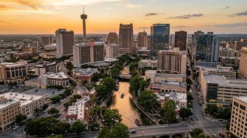 Aerial view of San Antonio's glowing skyline at golden hour with the river reflecting warm amber light below.