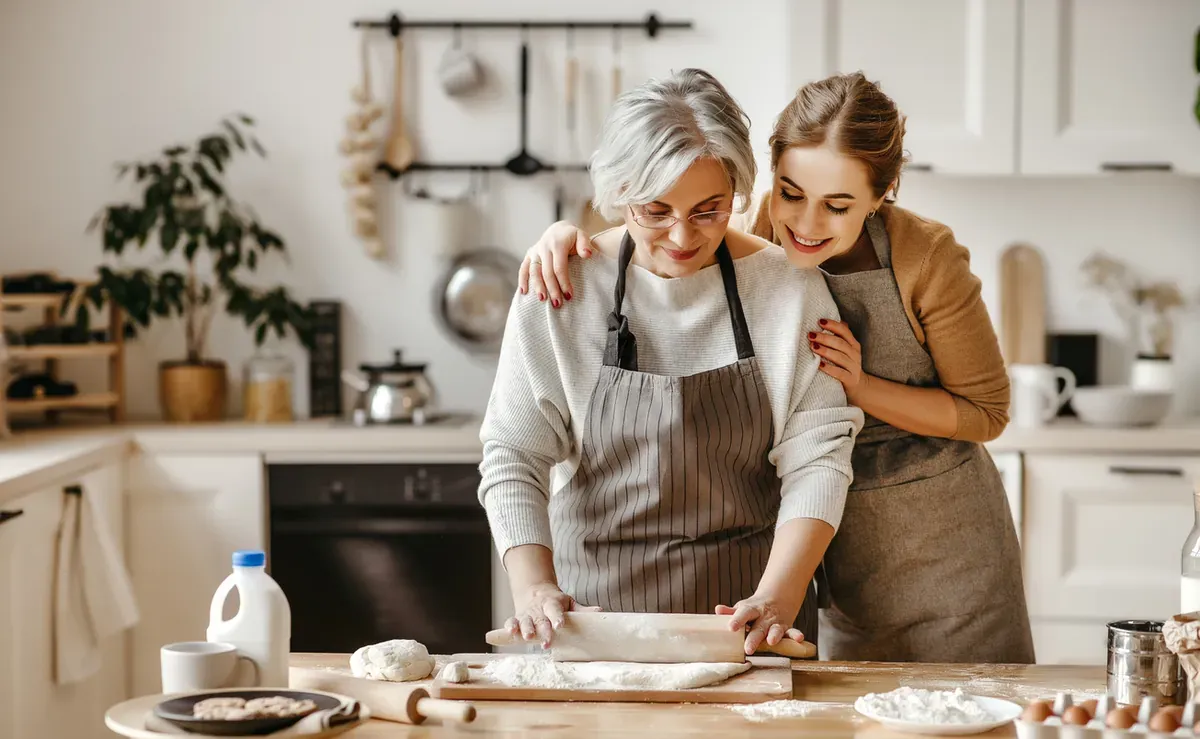 A woman and her mother-in-law cooking together in a bright kitchen.
