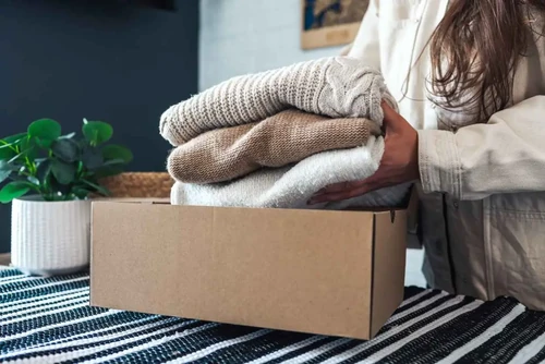 Box and woman putting folded up sweaters in it, storage for winter belongings, clothes