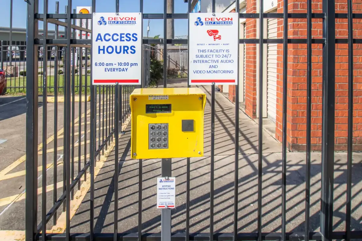 Keypad access system at Devon Self Storage gate with posted access hours and security monitoring signage