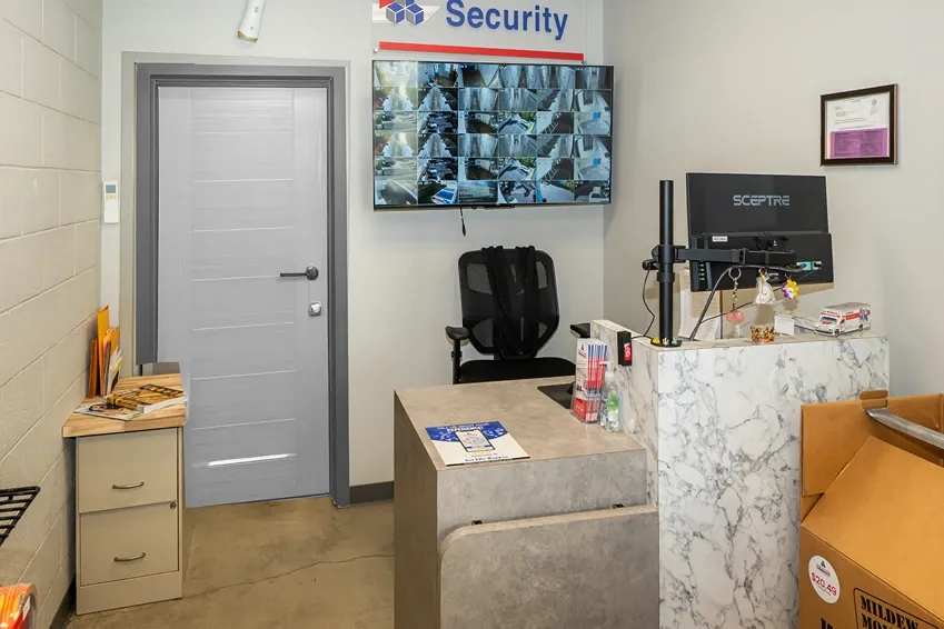 Self-storage front office with a marble-style counter, computer monitor, and wall-mounted multi-camera security display.