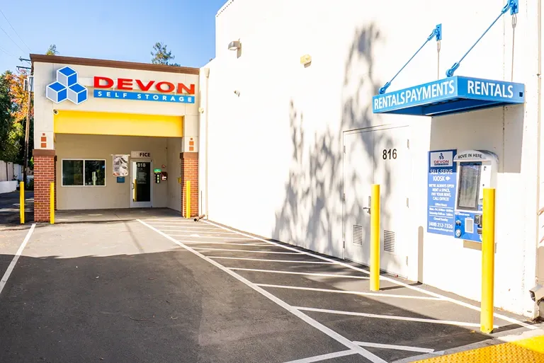 Exterior entrance of Devon Self Storage featuring branded signage, a drive-through entry, and a self-serve rental kiosk.