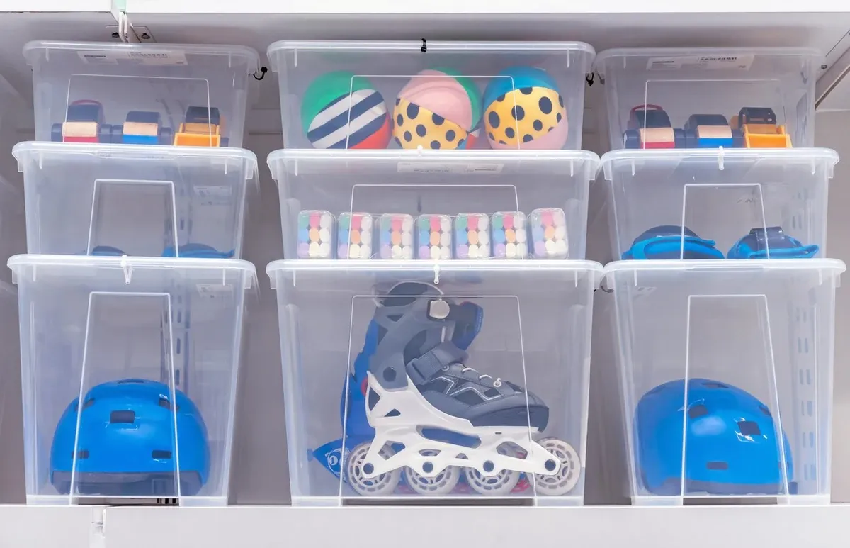 A group of clear plastic bins filled with sports equipment, toys, and other items neatly stacked on shelves.
