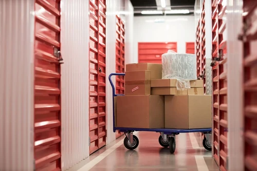 A cart with boxes on it sits outside of a row of self storage units.
