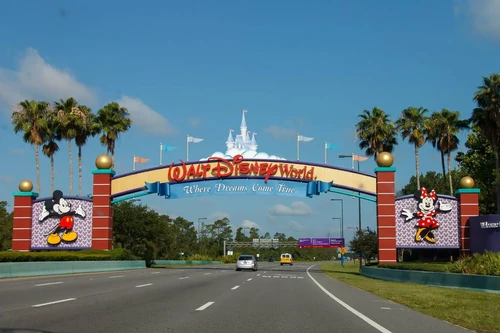 The iconic arched yellow and red sign at the entrance to Disney World in Orlando, FL, surrounded by palm trees.