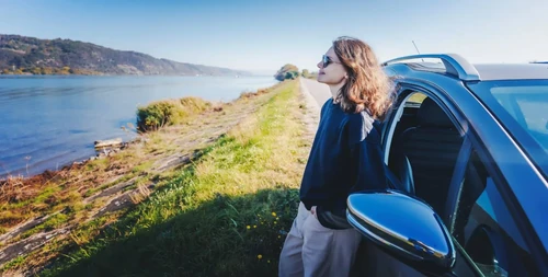 woman sitting up against her parked car, looking at water