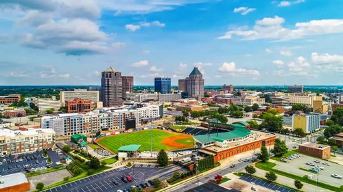 Aerial view of downtown Greensboro, NC, featuring the city skyline and a baseball stadium in the foreground.