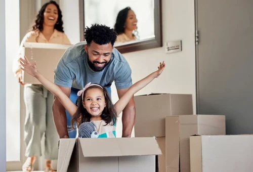 A father pushing his daughter in a moving box with her arms out.