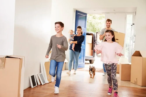 A happy family with a dog runs into their new home while moving.