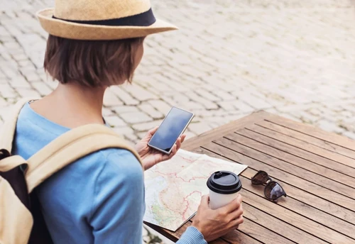 woman traveling, looking at her phone and map with coffee in the other hand