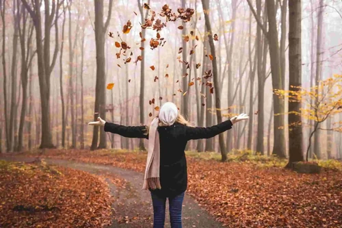 Woman standing on a walking path throwing up leaves