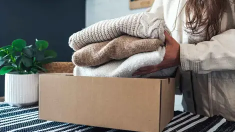 Box and woman putting folded up sweaters in it, storage for winter belongings, clothes