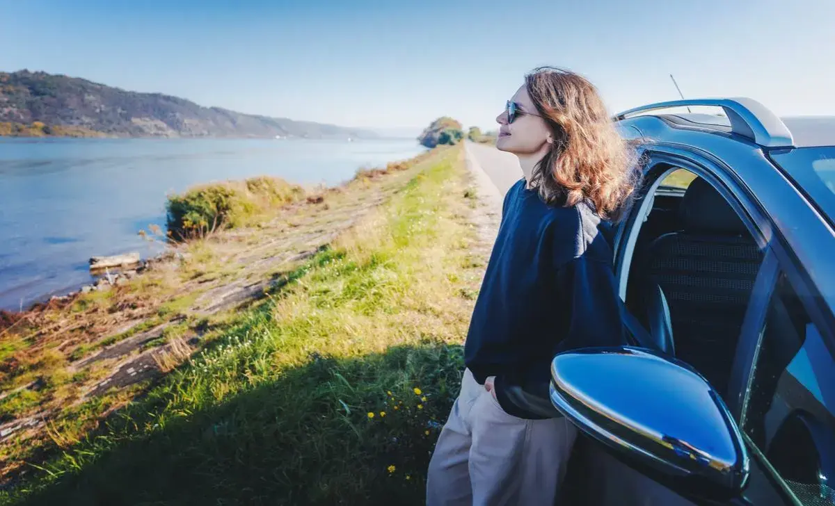 woman sitting up against her parked car, looking at water