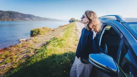woman sitting up against her parked car, looking at water