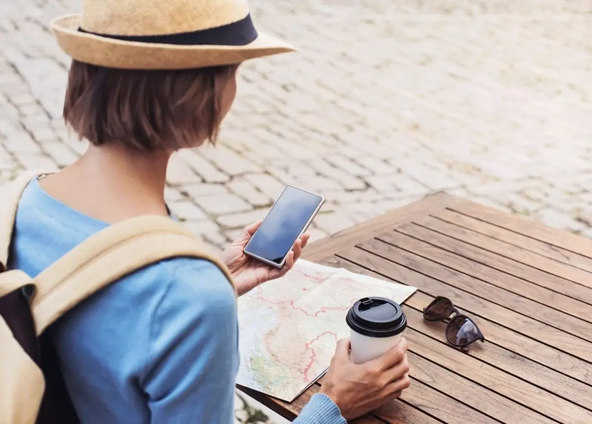 woman traveling, looking at her phone and map with coffee in the other hand