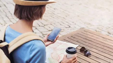 woman traveling, looking at her phone and map with coffee in the other hand