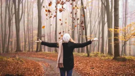 Woman standing on a walking path throwing up leaves