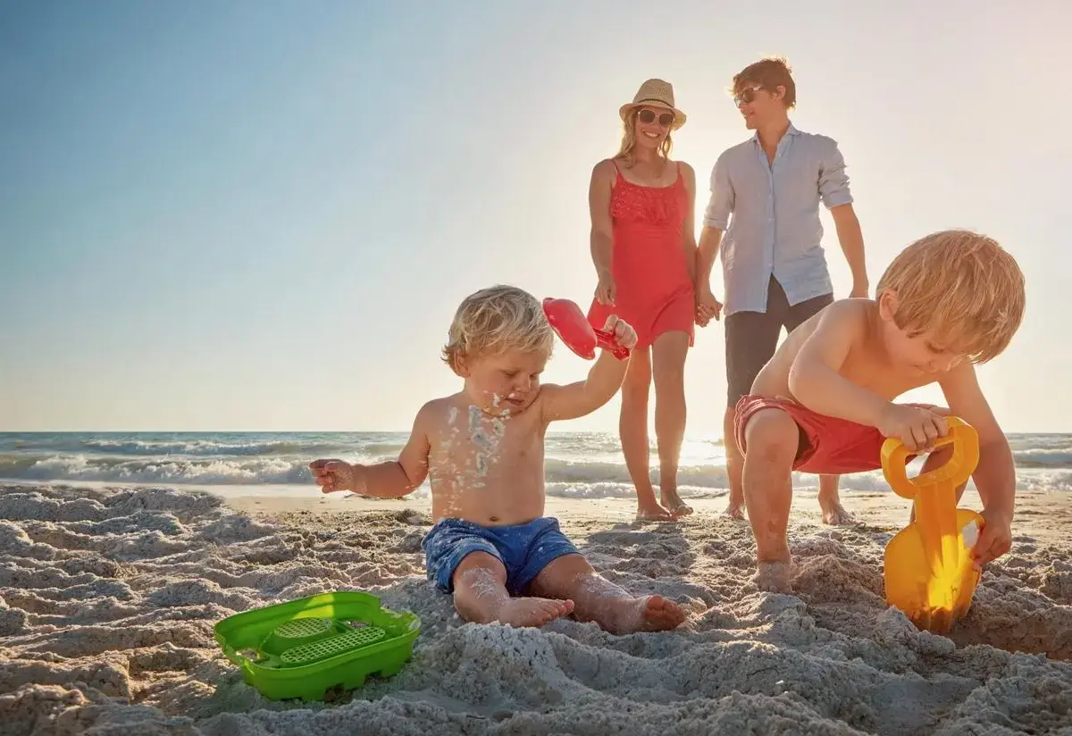 Parents watch their kids play in the sand on a beach vacation.