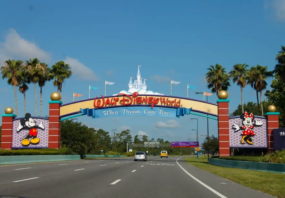 The iconic arched yellow and red sign at the entrance to Disney World in Orlando, FL, surrounded by palm trees.