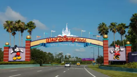 The iconic arched yellow and red sign at the entrance to Disney World in Orlando, FL, surrounded by palm trees.