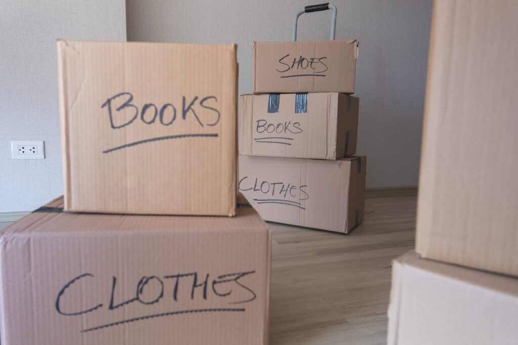Boxes labeled books, clothes, and shoes are stacked in an empty room.
