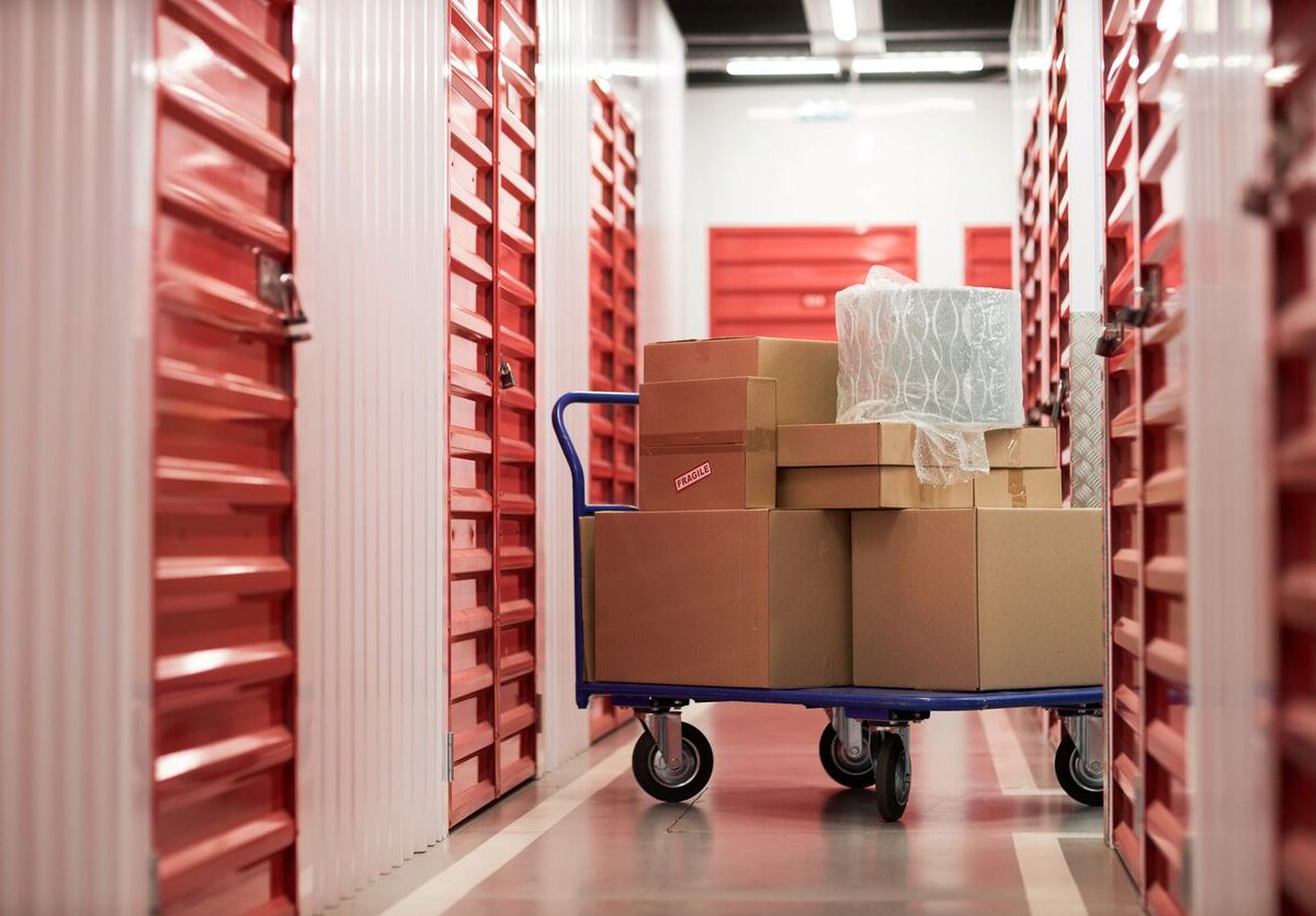 A cart with boxes on it sits outside of a row of self storage units.